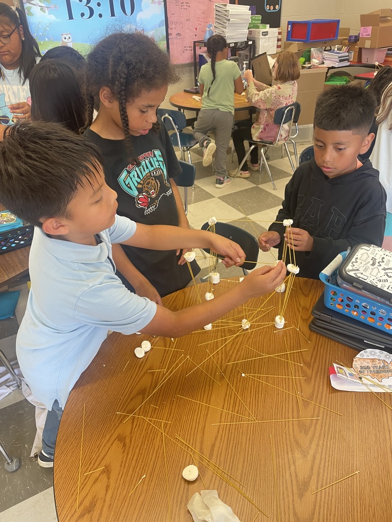 Three students are standing a table with their tower made from spaghetti and marshmallows.