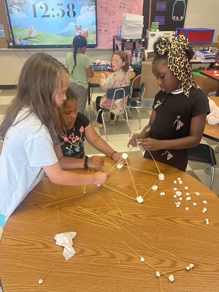 Three students are standing a table with their tower made from spaghetti and marshmallows.