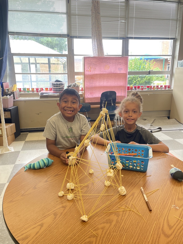 Two students are standing a table with their tower made from spaghetti and marshmallows.