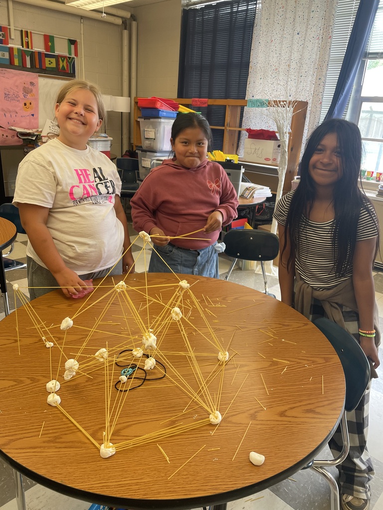 Three students are standing a table with their tower made from spaghetti and marshmallows.