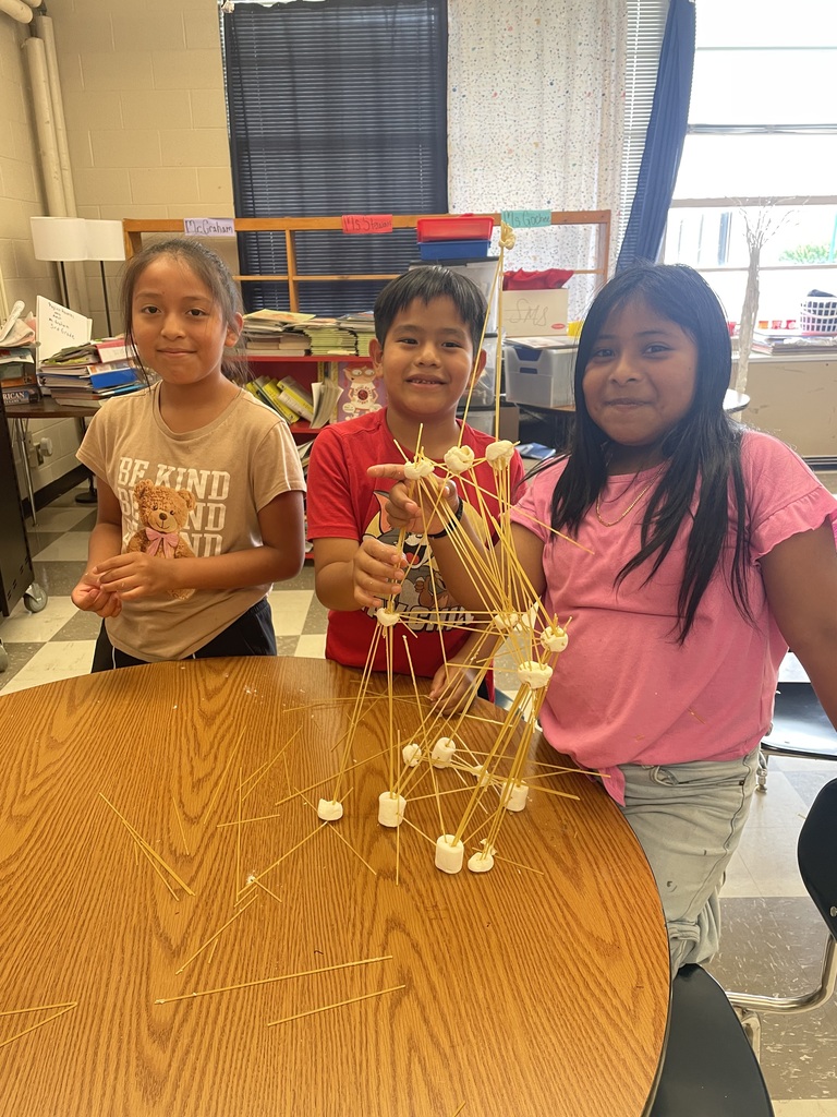Three students are standing a table with their tower made from spaghetti and marshmallows.