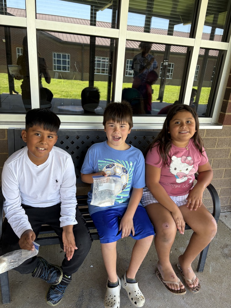 Three students are sitting on a bench and two of them are eating homemade ice cream from a bag.