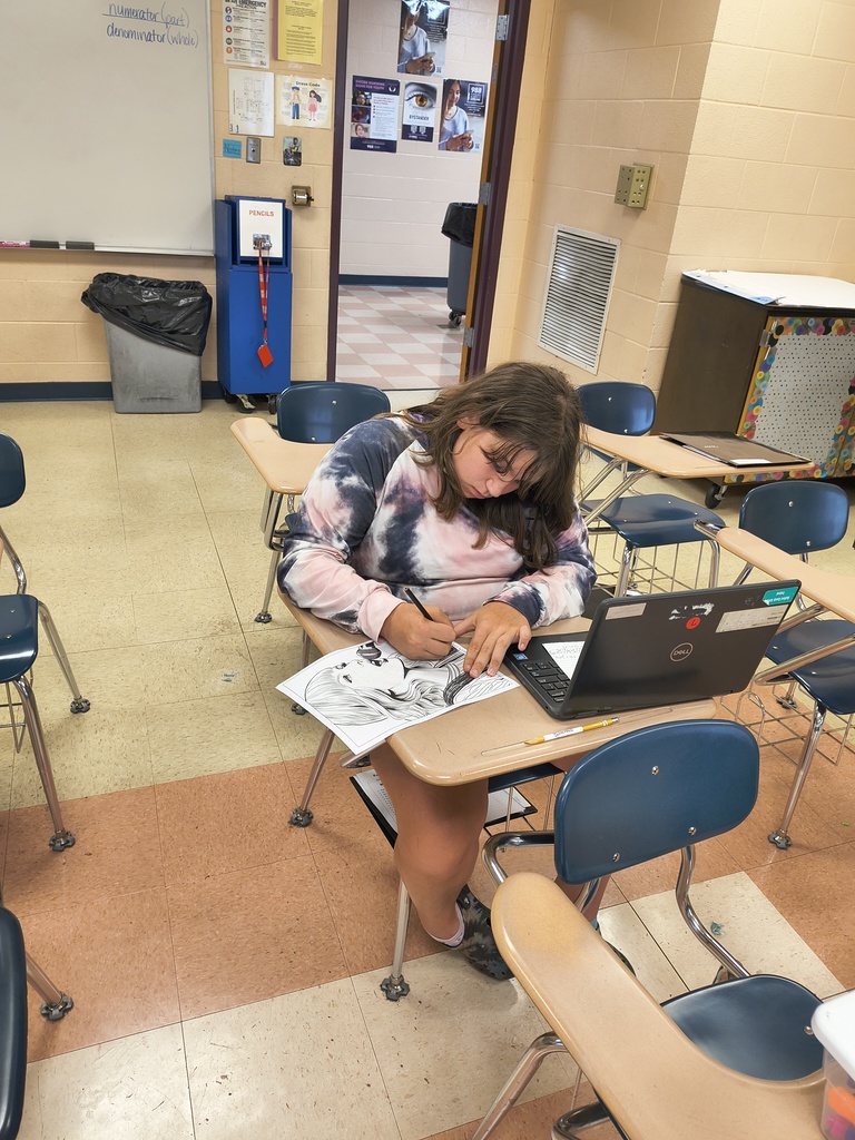 A student is sitting at a desk working on coloring in a drawing of a woman.
