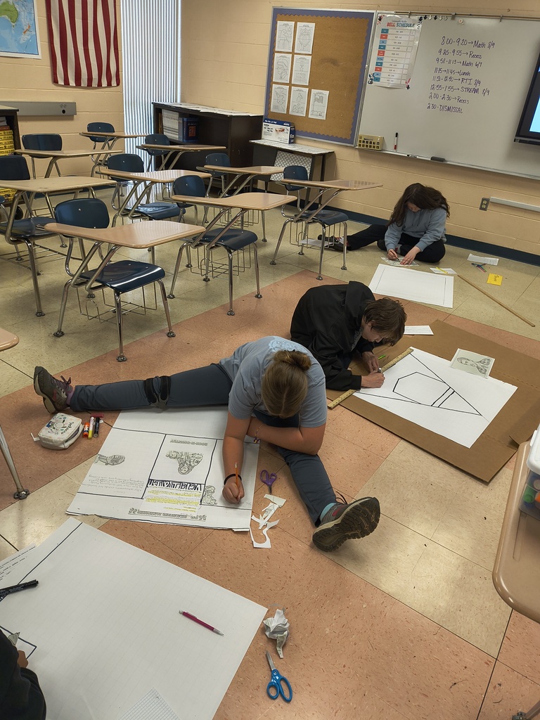 Three students are sitting in the floor with posters they are designing.