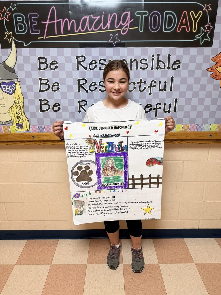 A student is standing in the hallway holding up the poster that they designed.