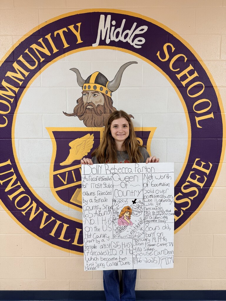 A student is standing in the hallway holding up the poster that they designed.