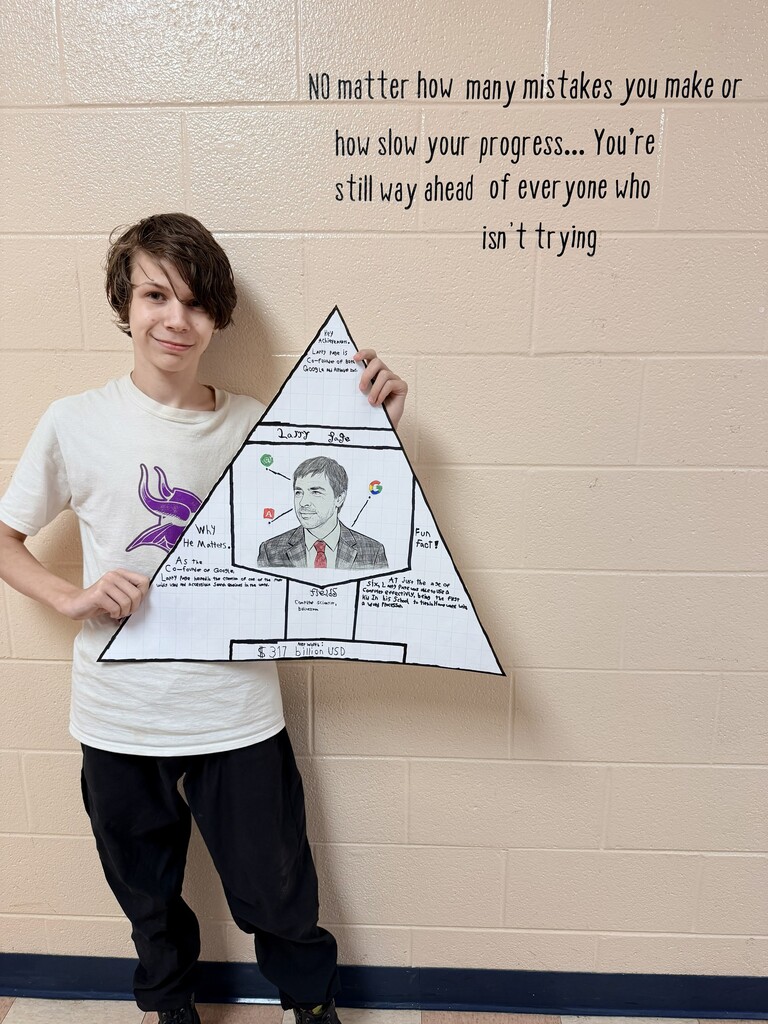 A student is standing in the hallway holding up the poster that they designed.