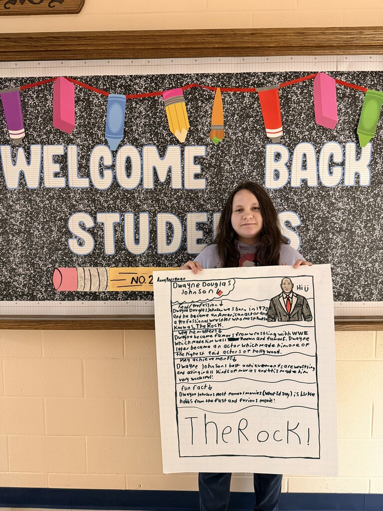 A student is standing in the hallway holding up the poster that they designed.