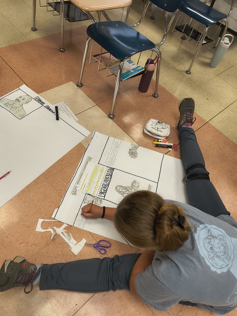 A student issitting in the floor with a poster she is designing.