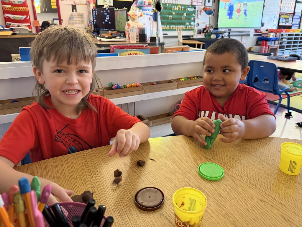 Two students are sitting at a table in their classroom playing with playdoh.