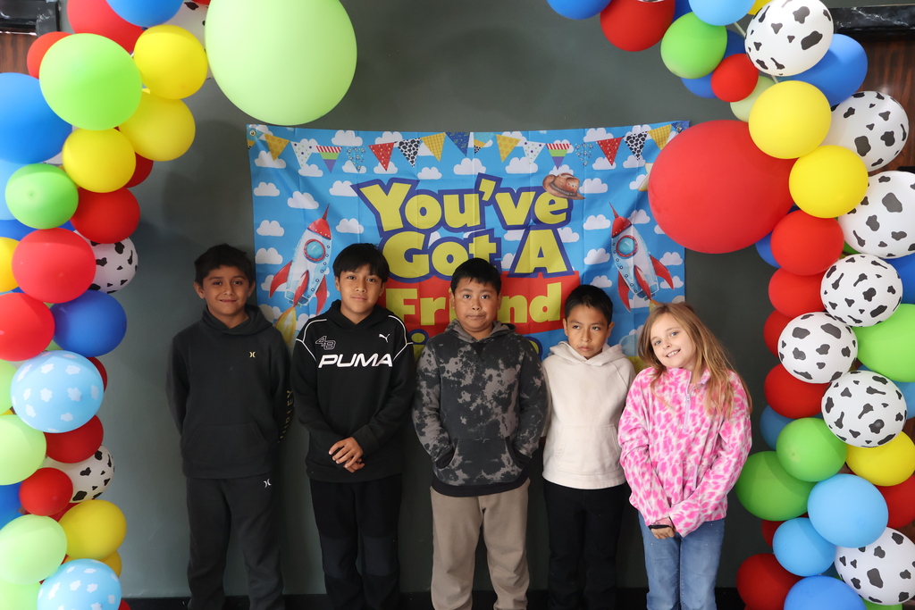 There are five students posed in front of a Toy Story themed backdrop with balloons. 