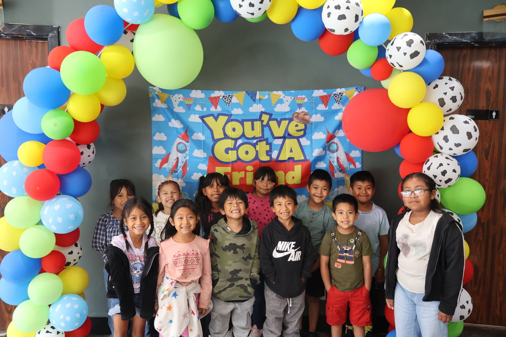 There are several students posed in front of a Toy Story themed backdrop with balloons. 