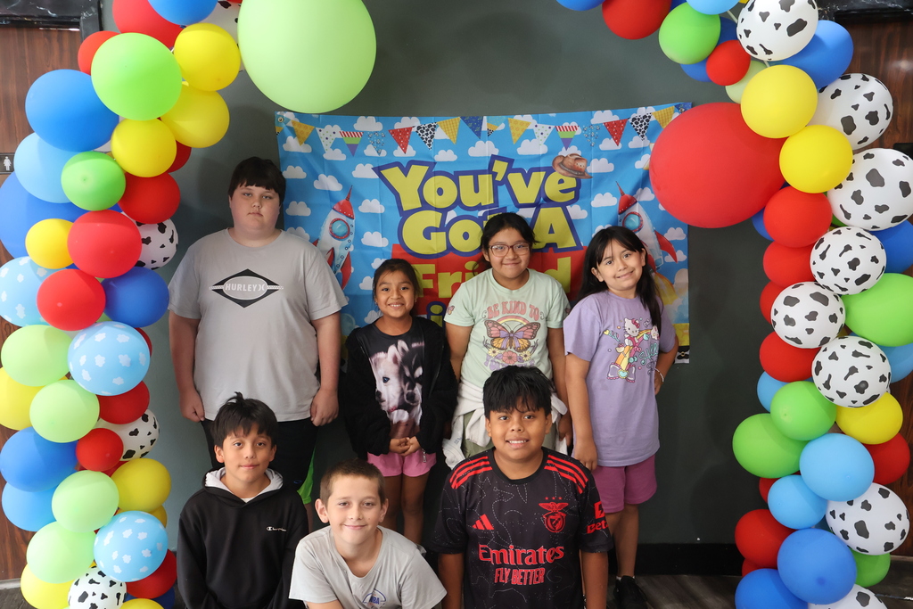 There are several students posed in front of a Toy Story themed backdrop with balloons. 