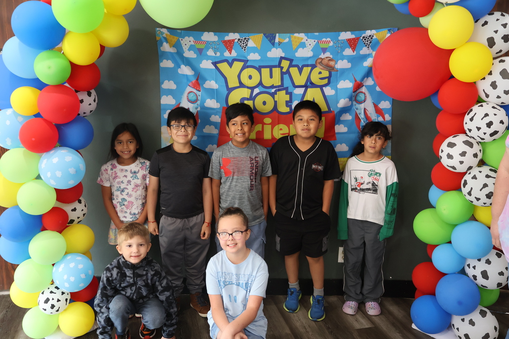 There are several students posed in front of a Toy Story themed backdrop with balloons. 