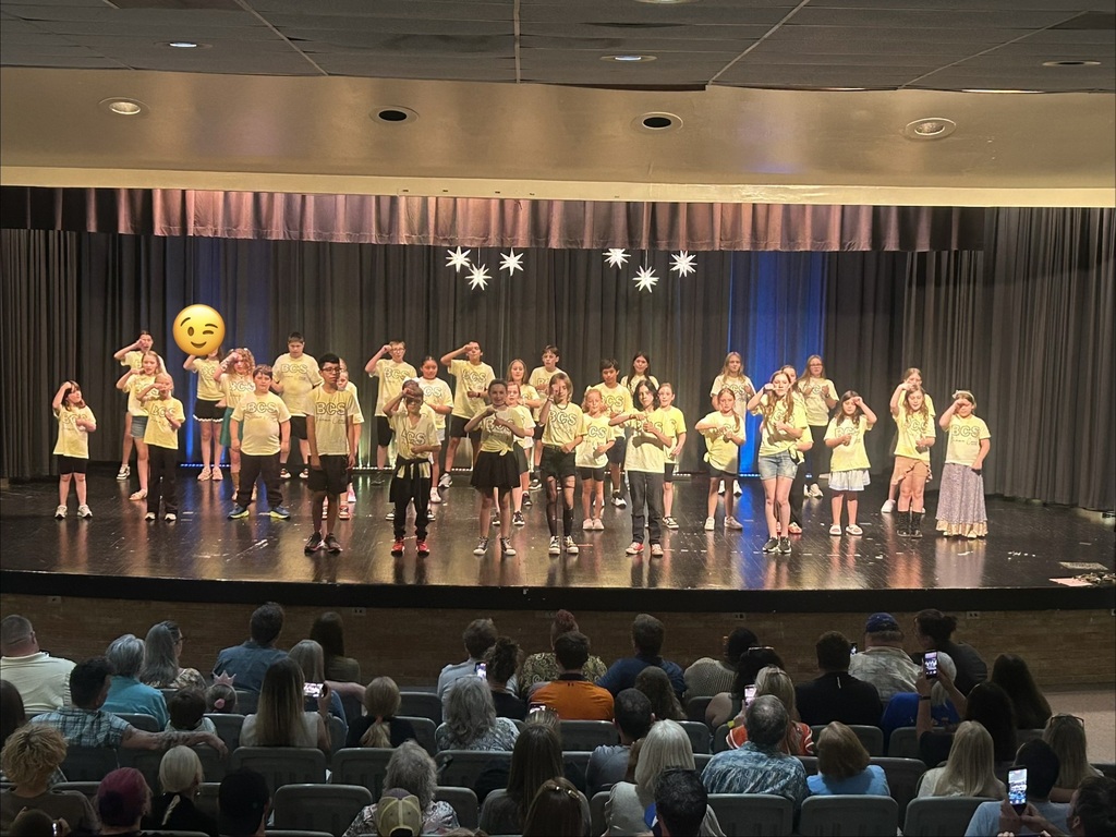 There is a group of students standing on a stage in the theater during their drama camp performance.