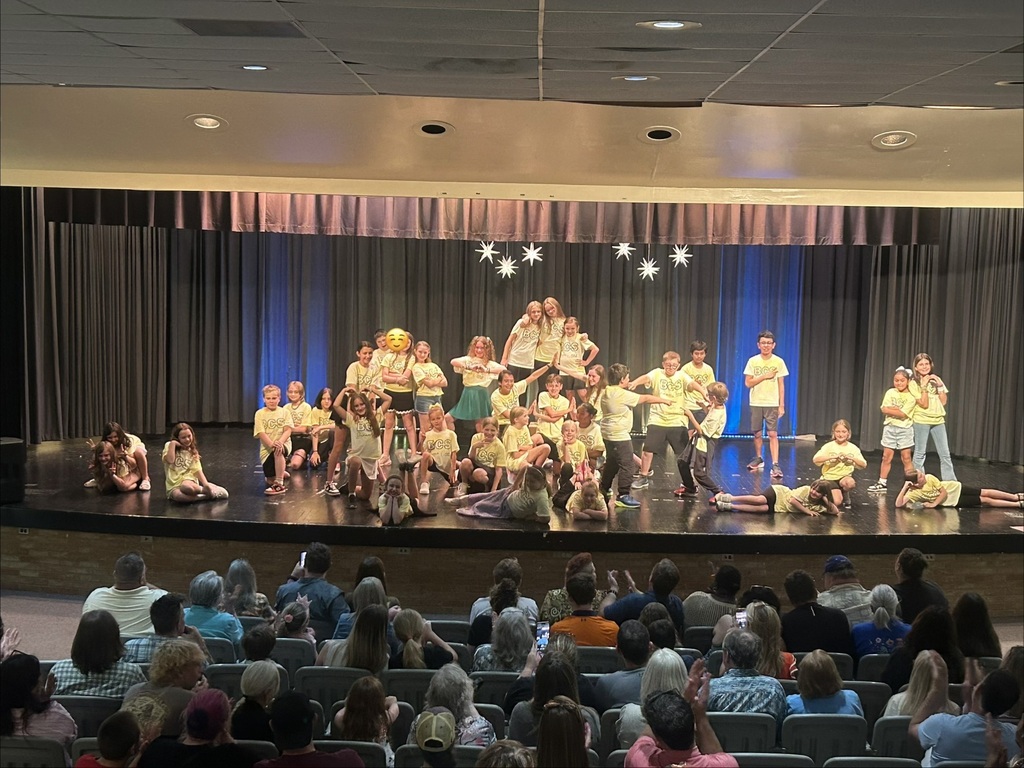 There is a group of students standing on a stage in the theater during their drama camp performance.