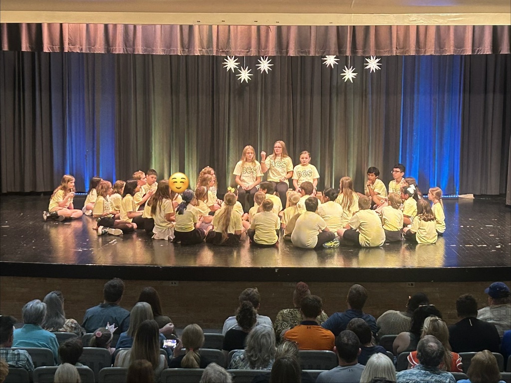 There is a group of students sitting on a stage in the theater during their drama camp performance.