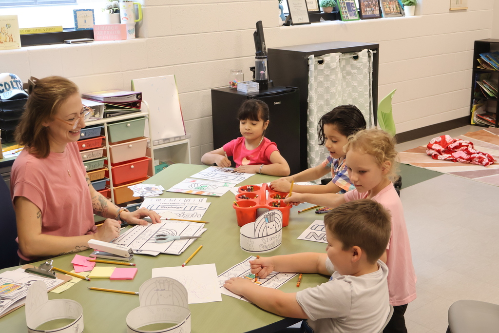 Thare are four students sitting at a table with their teacher doing work.