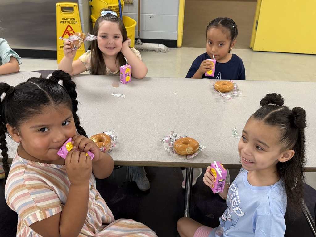 Four students are sitting at a cafeteria lunch table as they enjoy donuts and juice boxes. 