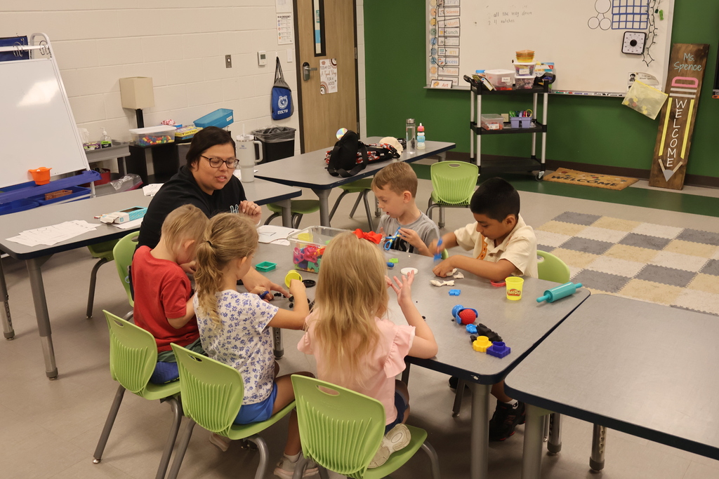 There are five students sitting at a table with a teacher playing with play doh.