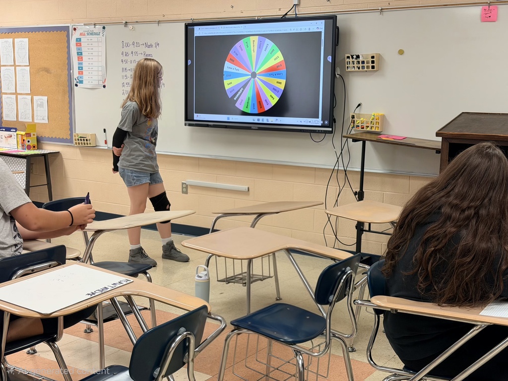 A student is standing in the classroom playing wheel of fortune on the board. 