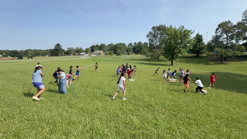 Students are outside playing in the grass with water balloons and other water toys. 