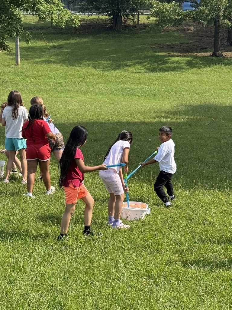 Students are outside playing in the grass with water balloons and other water toys. 