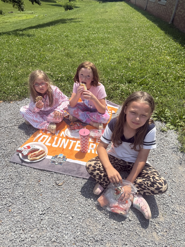 Three students are sitting on a blanket outside eating their hotdogs and chips. 