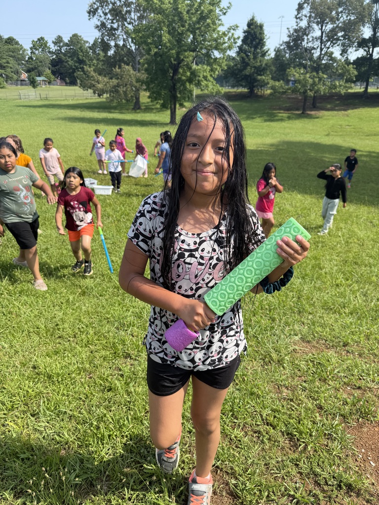 A student is holding a water toy in her hands as other students are playing behind her.