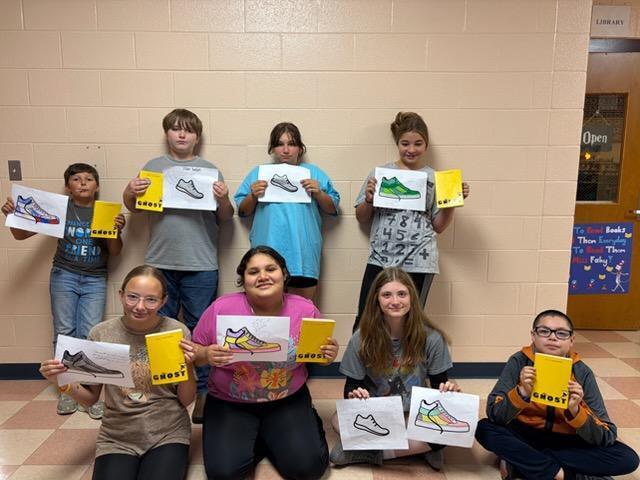 Students are standing in the hallway posed for a picture holding up the book they have all been reading. 