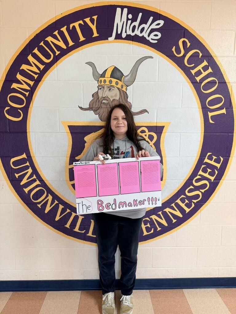 A student is standing in the hallway holding up the poster that they designed. 