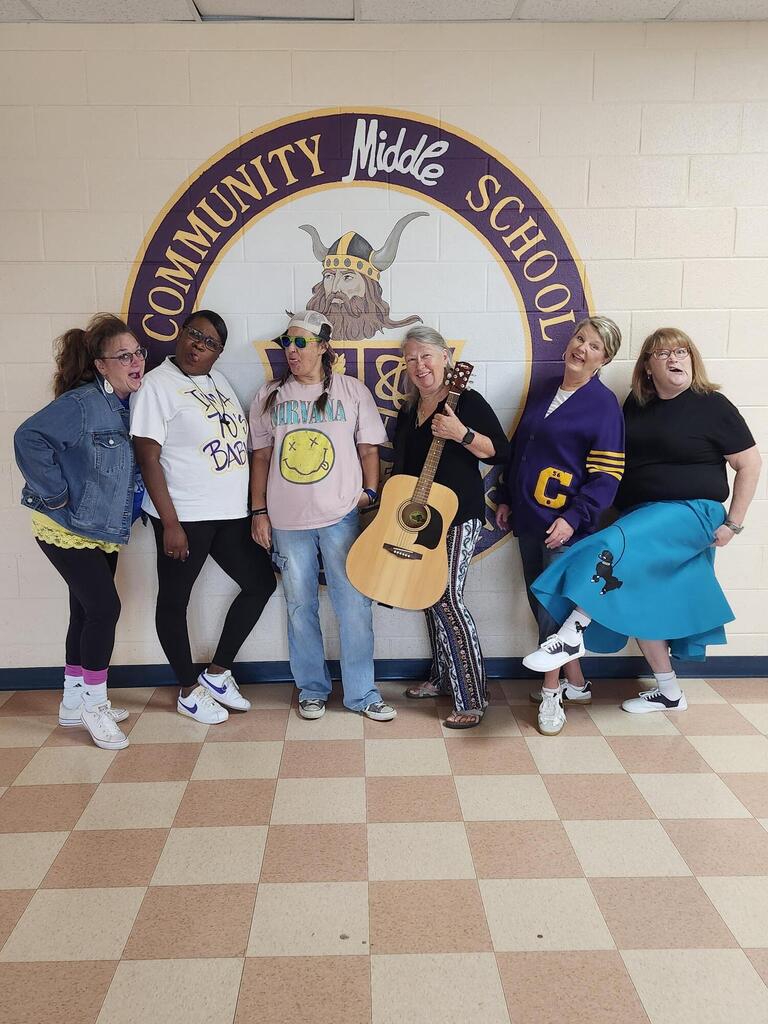 Six teachers are standing in the hallway posed for a picture wearing their outfits for "decades day". 