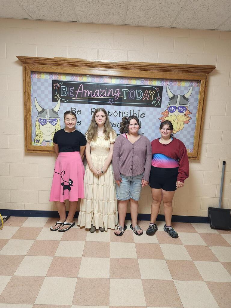 Four students are standing in the hallway posed for a picture wearing their outfits for "decades day". 