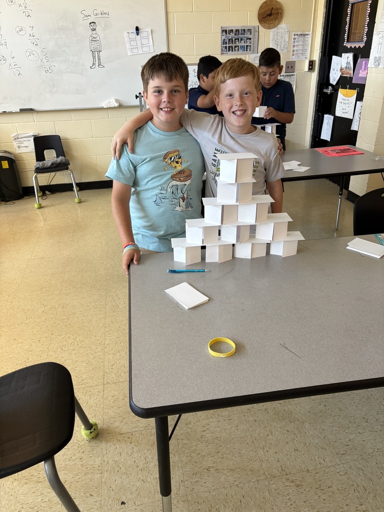 Two students pose for a picture in front of the tower they created out of index cards. 
