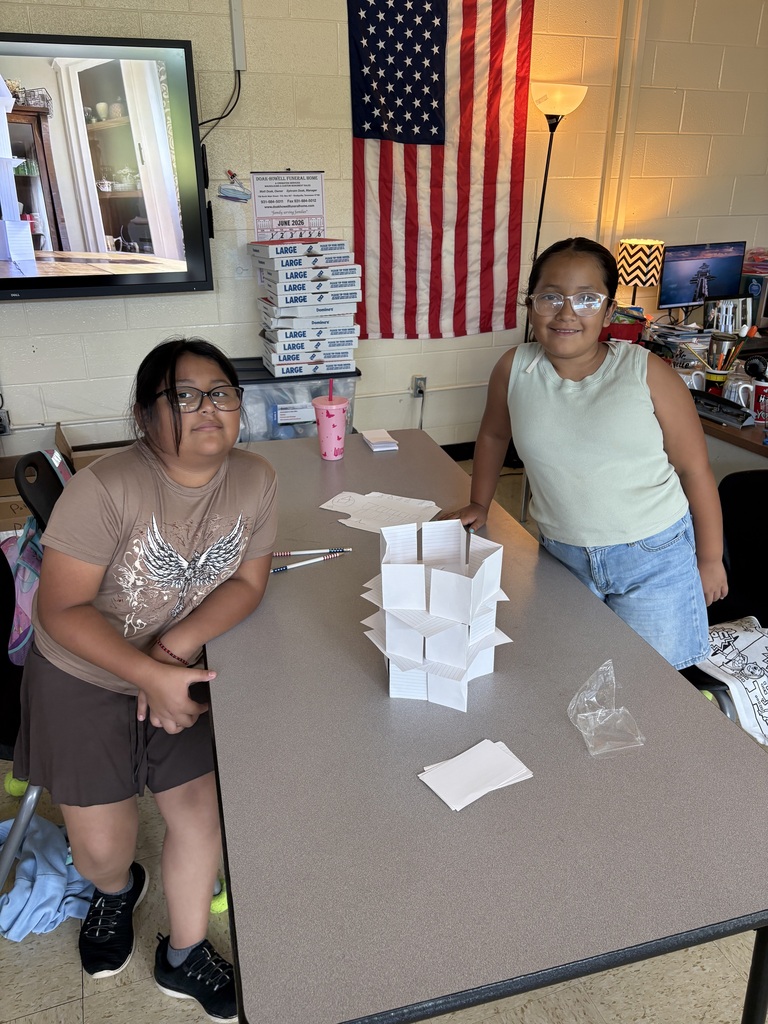 Two students pose for a picture in front of the tower they created out of index cards. 