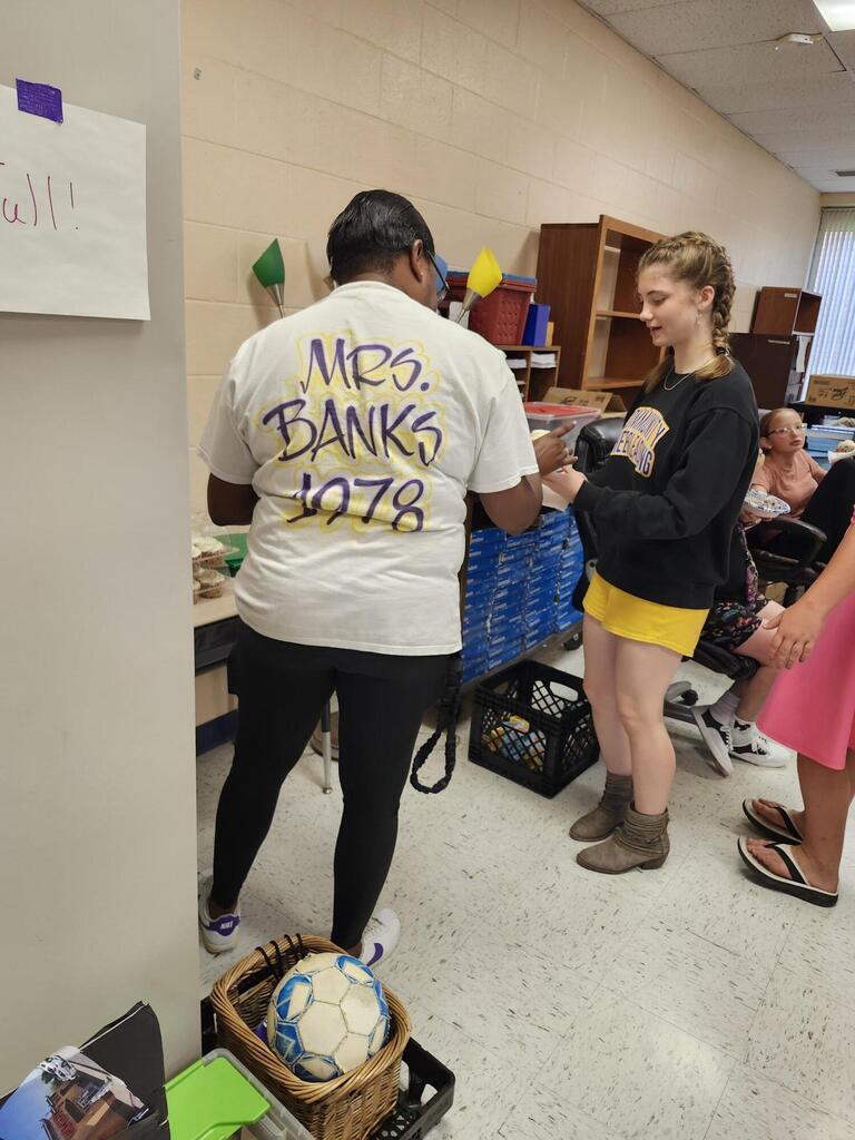 There is a teacher in this picture handing a student a cupcake. 