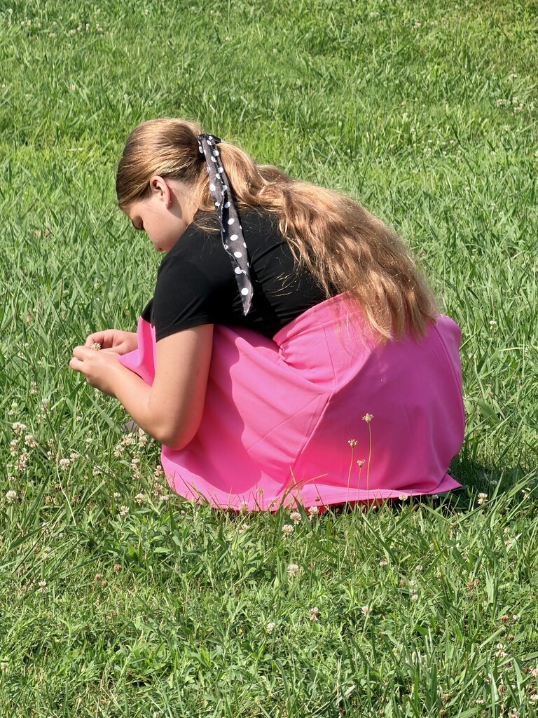 A student is kneeling down outside picking flowers in the grass. 