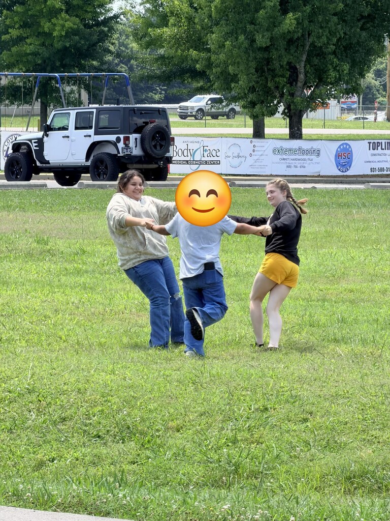 There are three students holding hands going in a circle outside. 