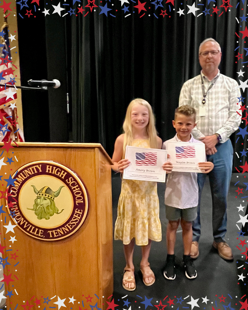 Two students hold up a certificate beside the assistant superintendent after saying the pledge of allegiance before the board meeting.