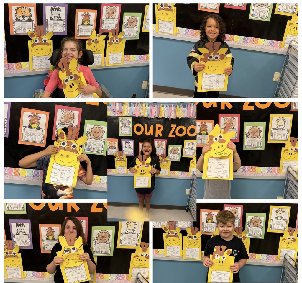 There are several students holding up a piece of construction paper that they designed as a giraffe. 