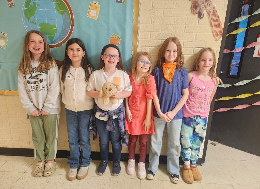 There are six girl students standing in the hallway smiling for a group picture.