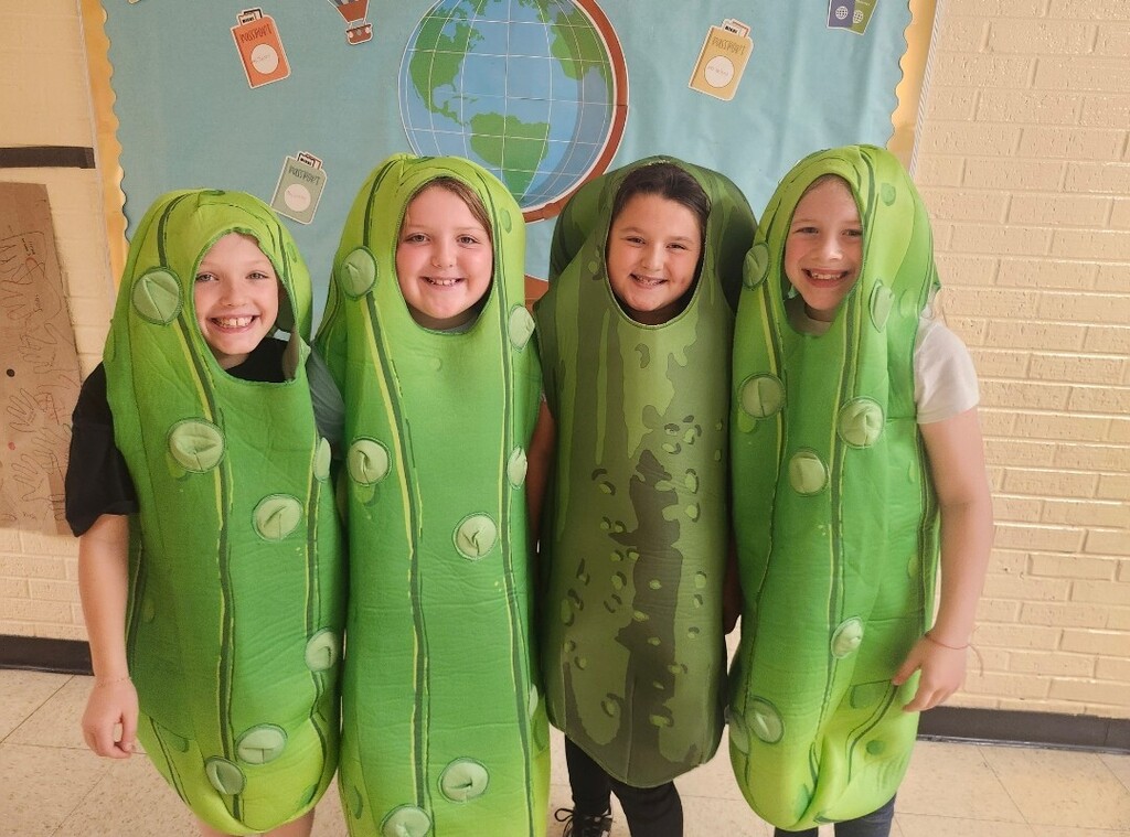 There are four students standing in the hallway dressed in costumes that look like pickles.