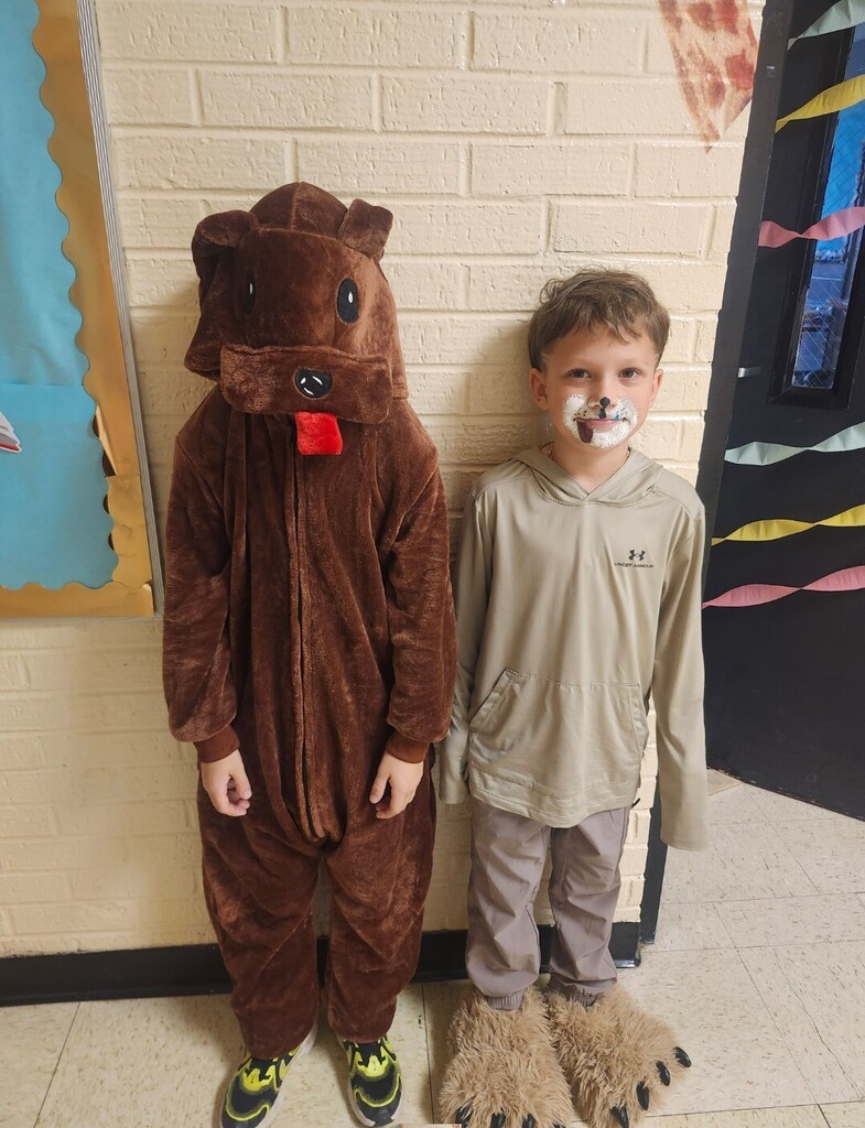 A student is in a dog costume standing beside another student for a picture in the hallway.