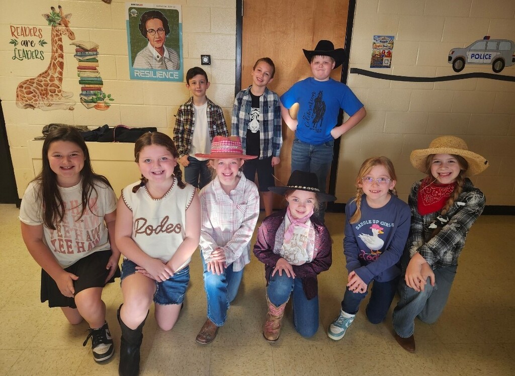 There is a group of students posed in the hallway wearing western wear with cowboy hats and boots.
