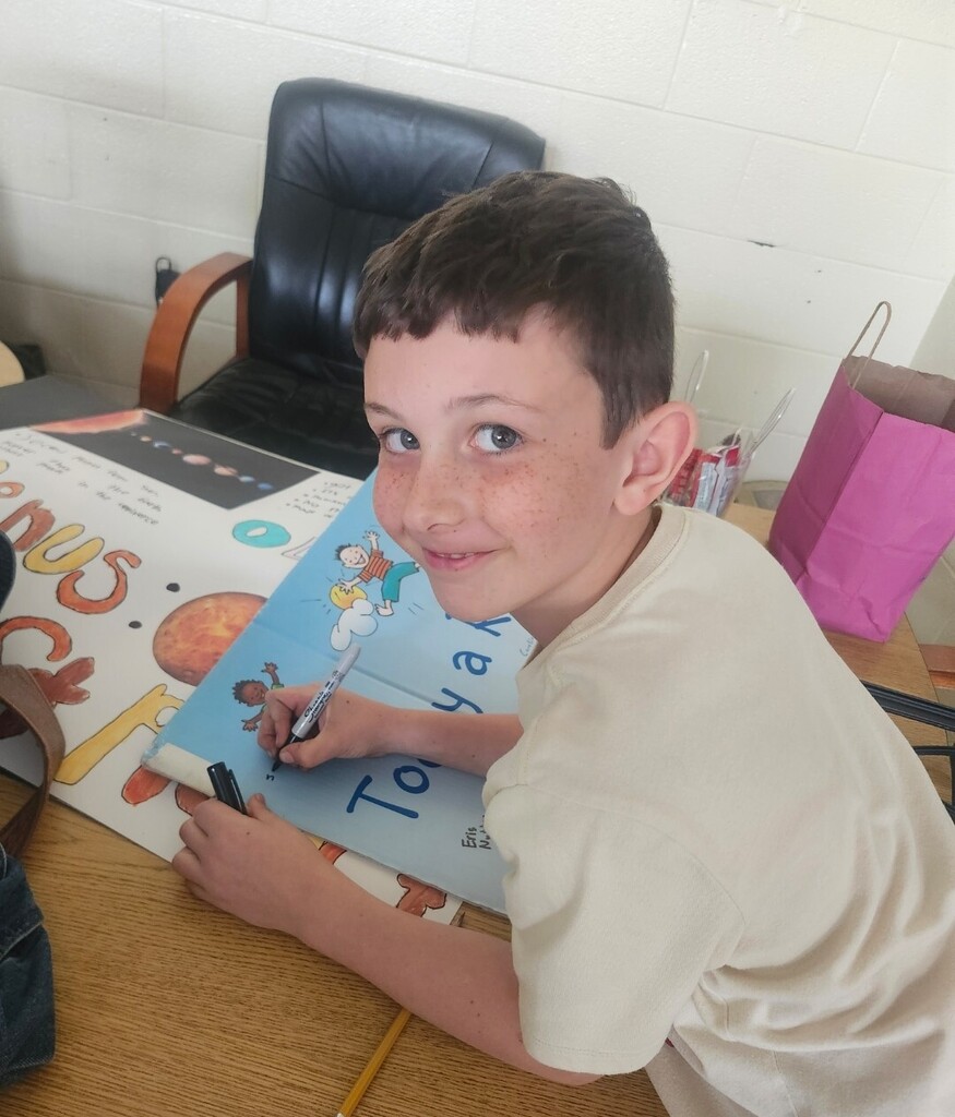 A student is smiling and writing on a large poster board.