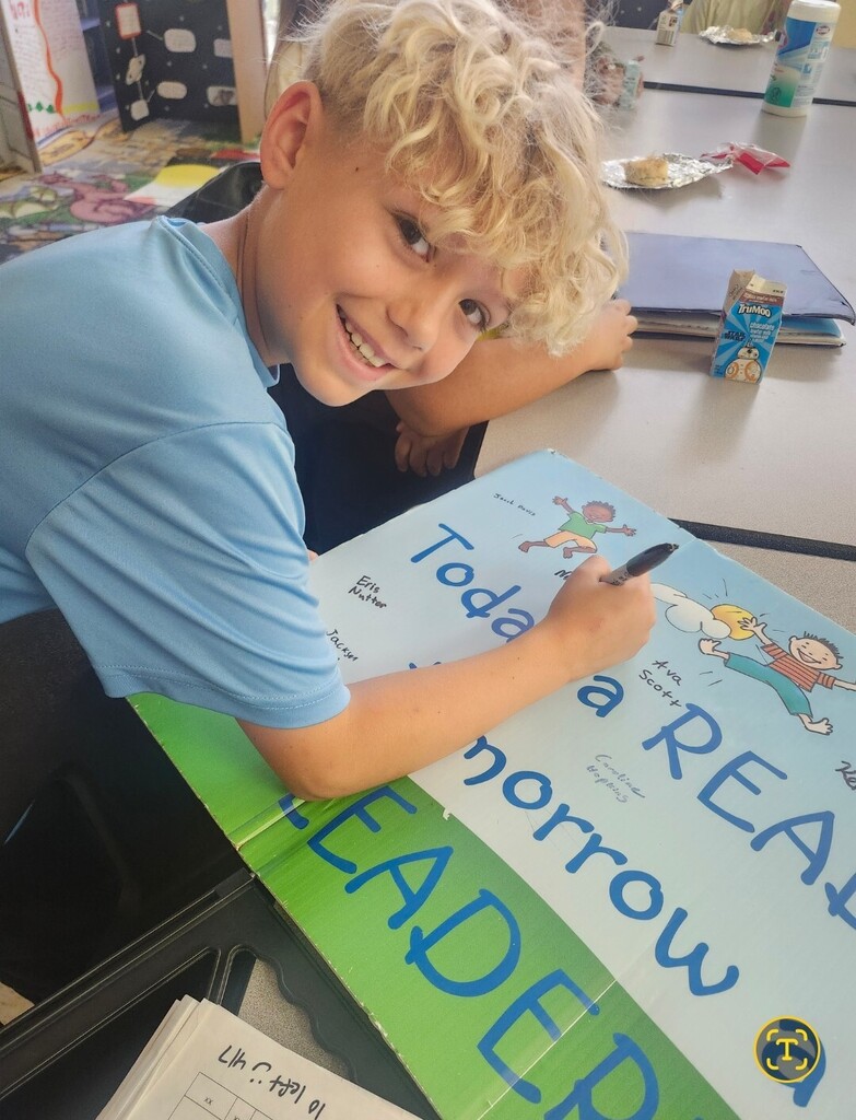 A student is smiling and writing on a large poster board.