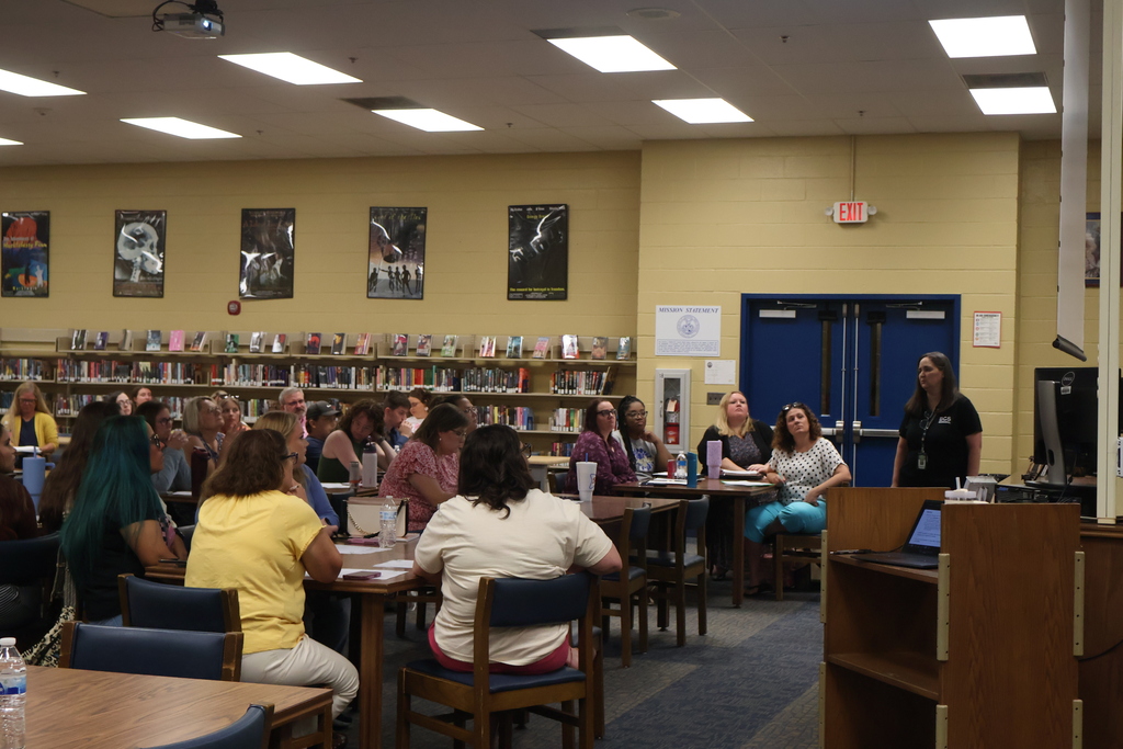 The supervisor of the Technology Department speaks to a library full of people seated at tables. 