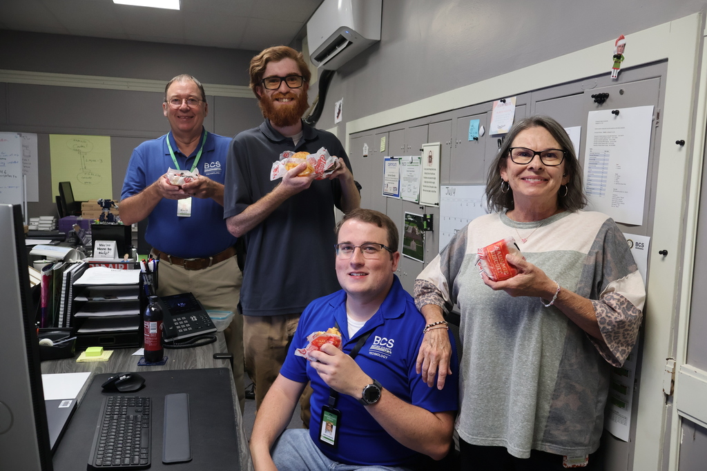 There are four people who are posed for a picture each holding a sausage biscuit from Hardee's.