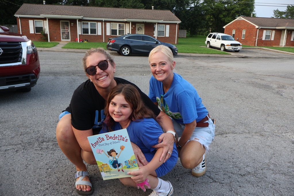 The principal and assistant principal are both posed for picture with a student as she is holding a book. 