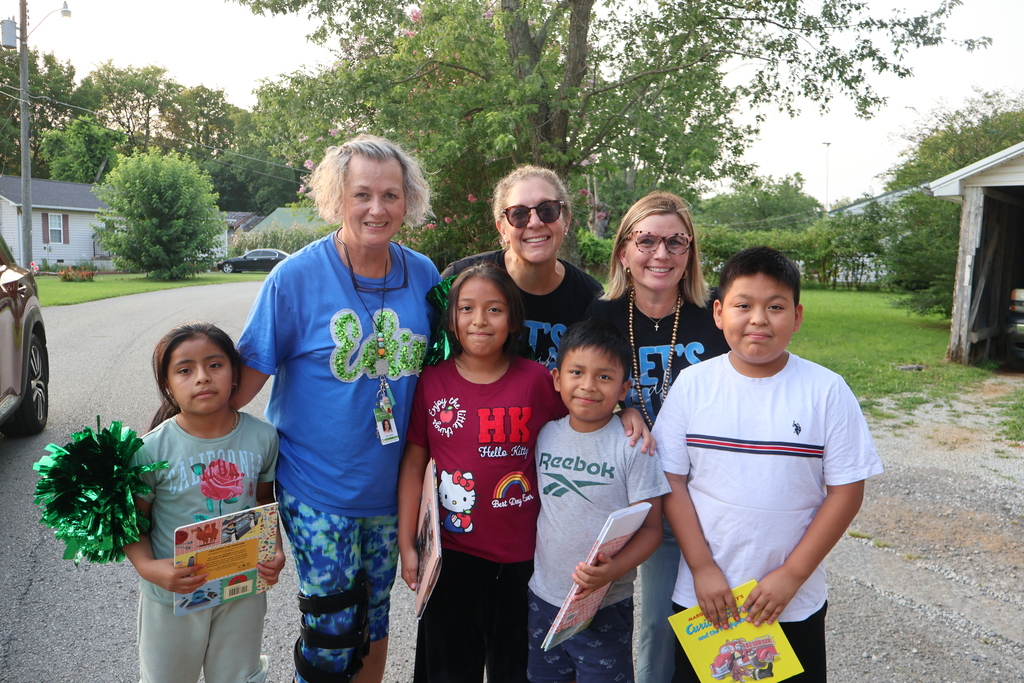 The principal and two teachers are all posed for a group picture with four students who are each holding a book in their hands. 